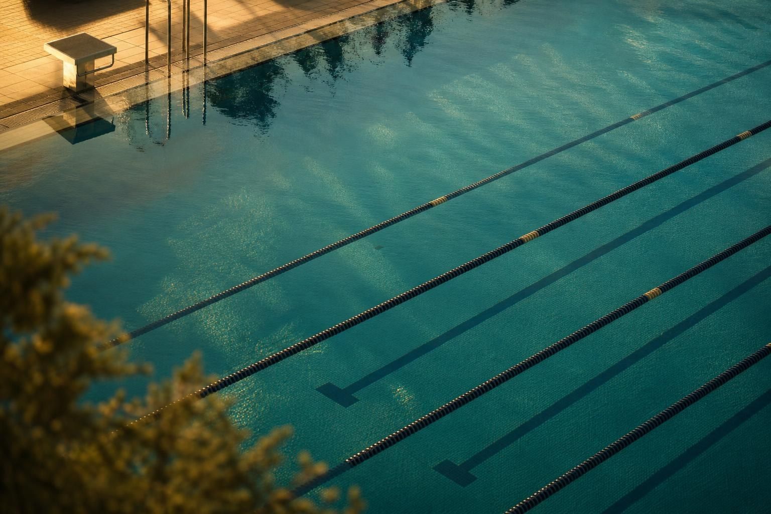 A swimming pool seen from above, with lane ropes and calm turquoise water in early morning light (AI-generated image)